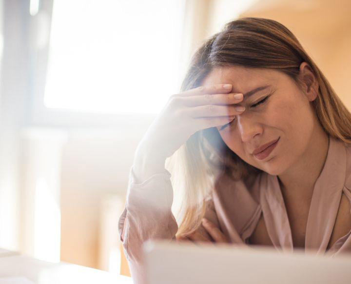 Woman with migraine symptoms from light sensitivity while sitting at her laptop